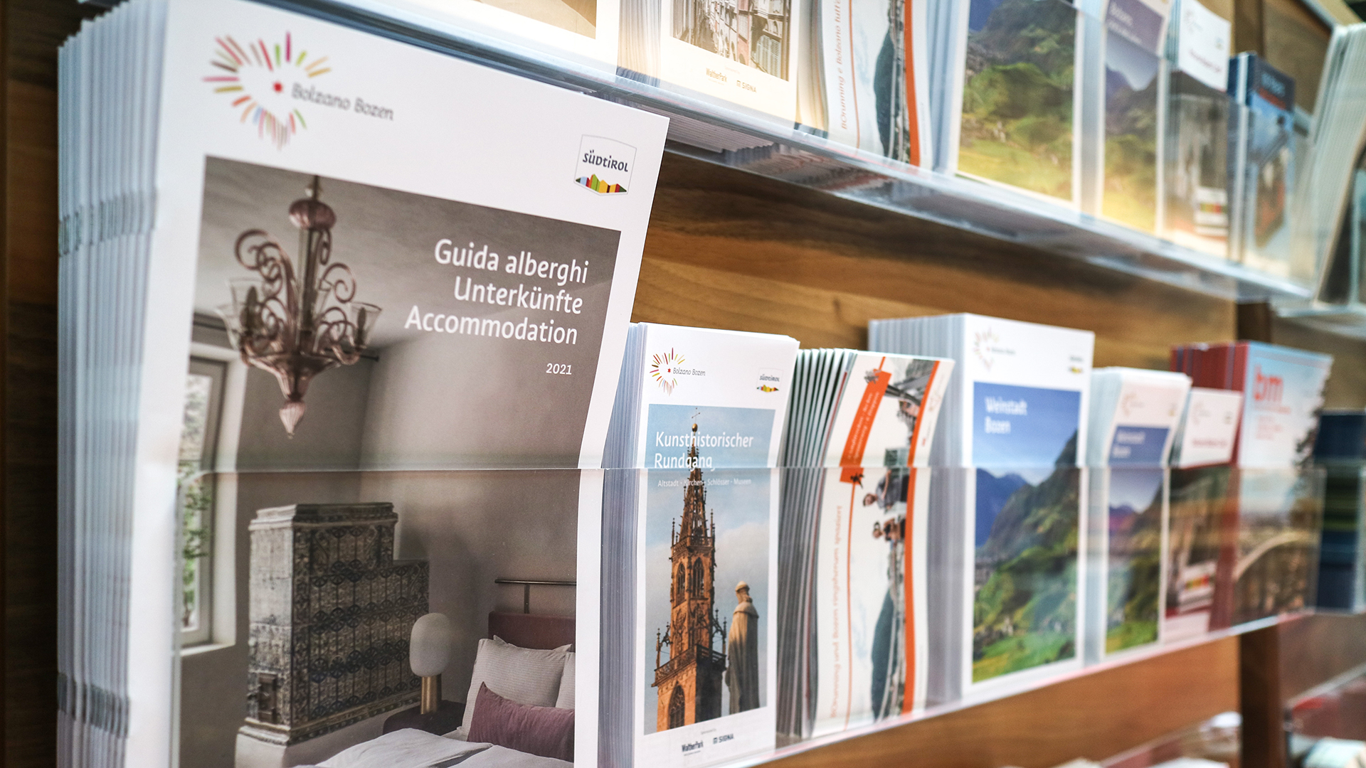 Volantini e itinerari poggiati sugli scaffali degli uffici informativi permettono ai turisti di trovare l'ispirazione su quale punto di interesse a Bolzano visitare nelle loro vacanze.